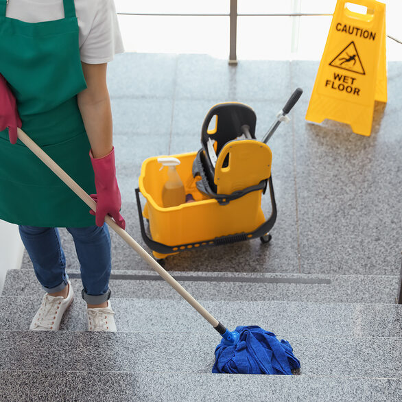 Young woman with mop cleaning stairs indoors